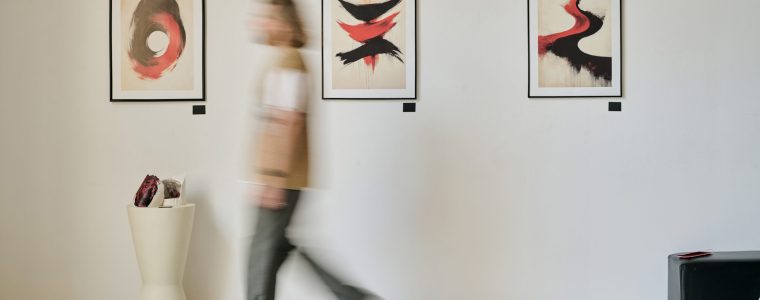 Blurred figure walking through art gallery exhibiting abstract paintings on wall demonstrating motion. Artwork showcasing dynamic brushstrokes and vivid contrasts